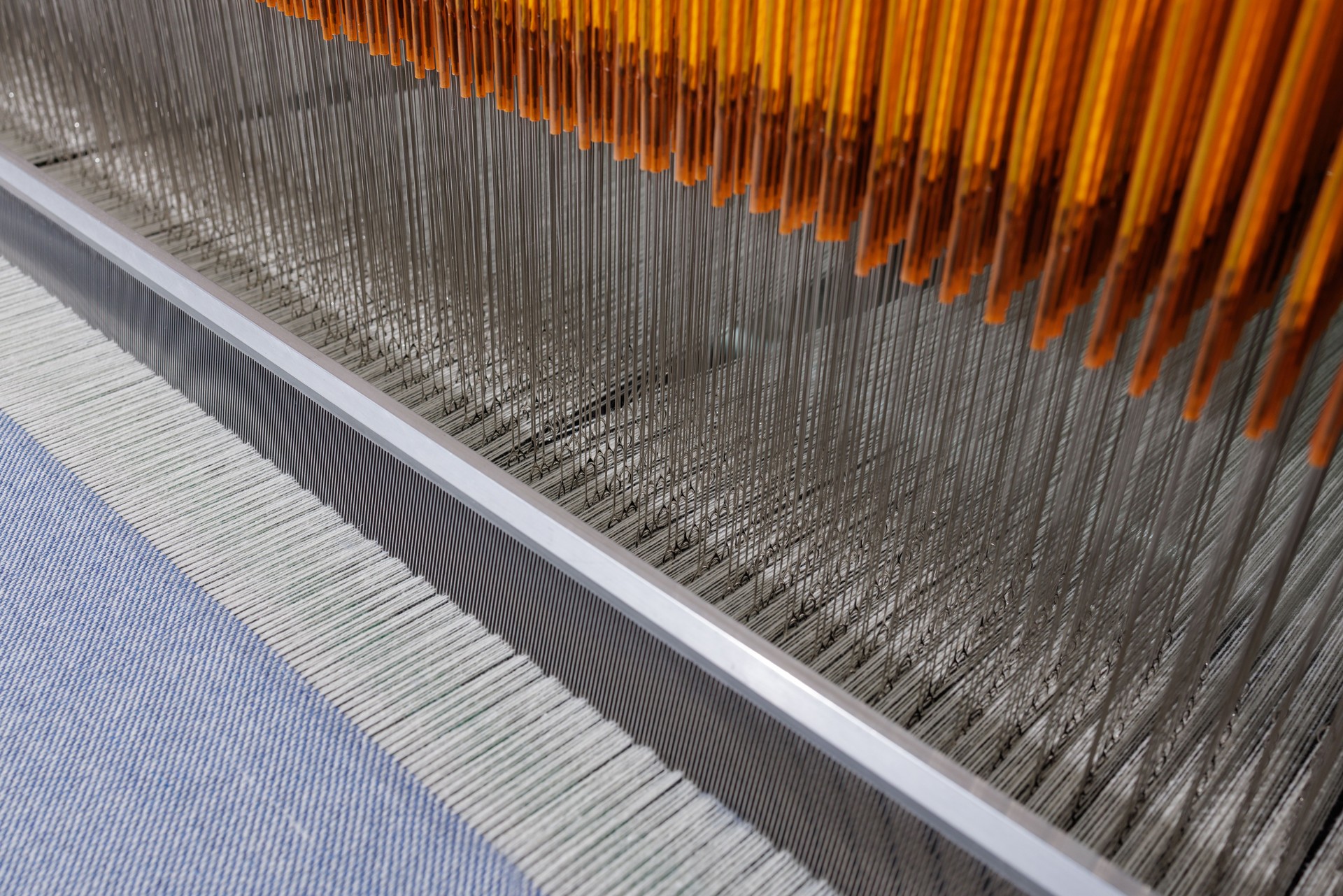 Detail of textile weaving machine with threads, loom operation in fabric manufacturing process.